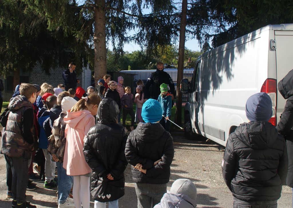 grupa dzieci i policjant podczas scenki szukania łądunku wybuchowego 