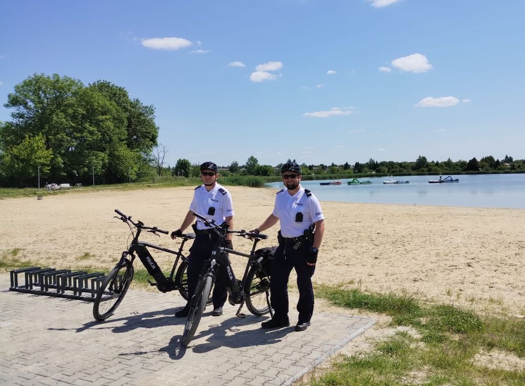 dwóch policjantów stojących przy rowerach służbowych, w tle akwen wodny