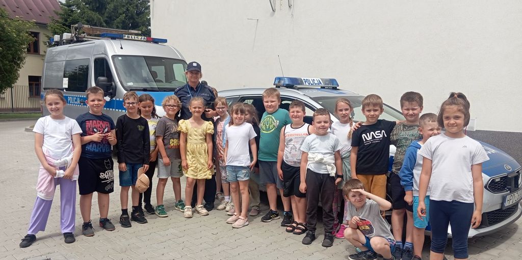 dzieci z policjantką przed radiowozami  