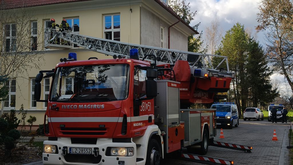 ćwiczenia, budynek szkoły przed którym stoi wóz strażacki i radiowóz 