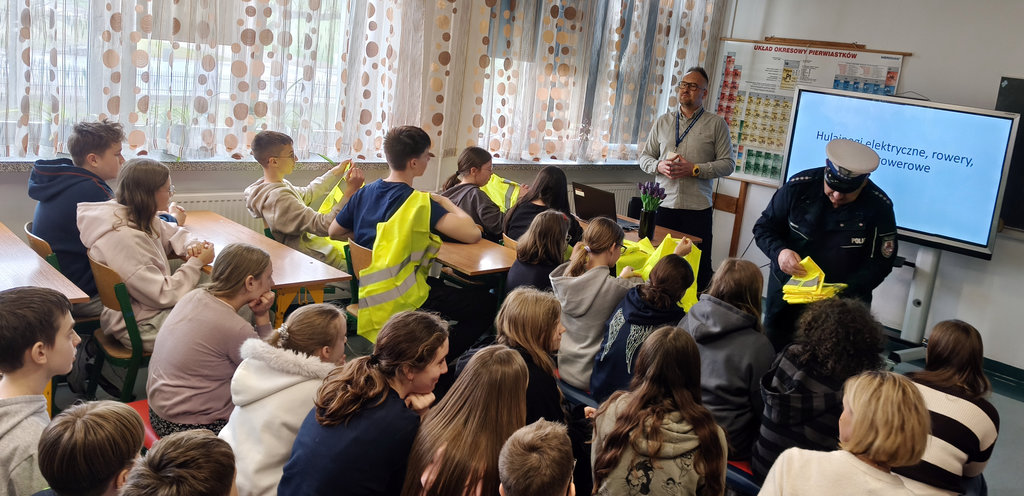 policjant rozdaje uczniom kamizelki odblaskowe