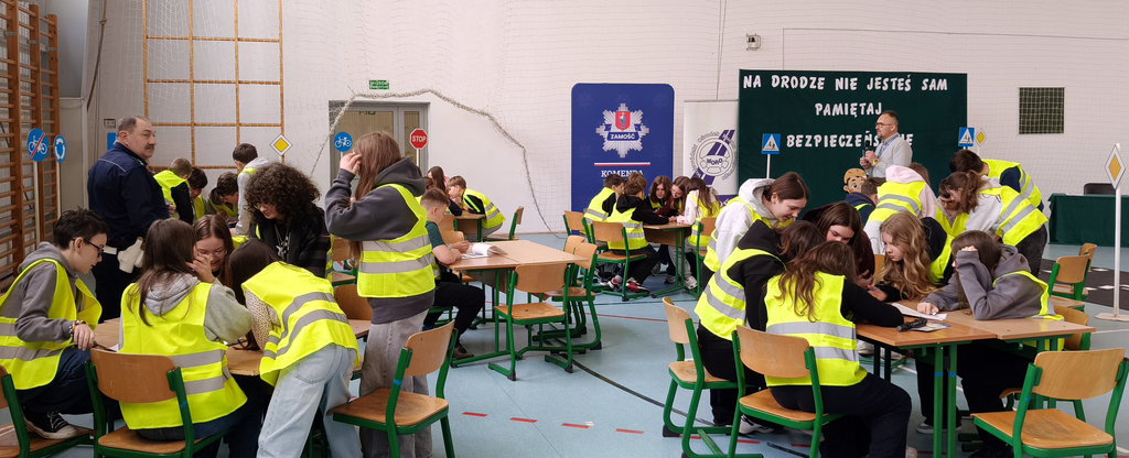 młodzież siedząca przy stolikach rozwiązuje test wiedzy