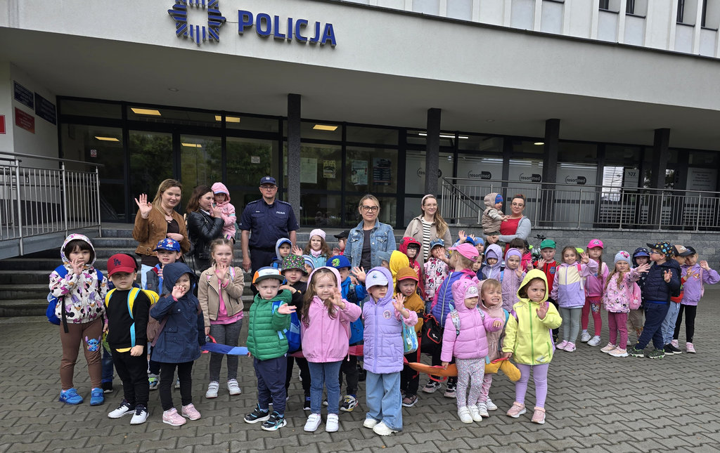 zdjęcie grupowe dzieci z policjantem przed budynkiem komendy