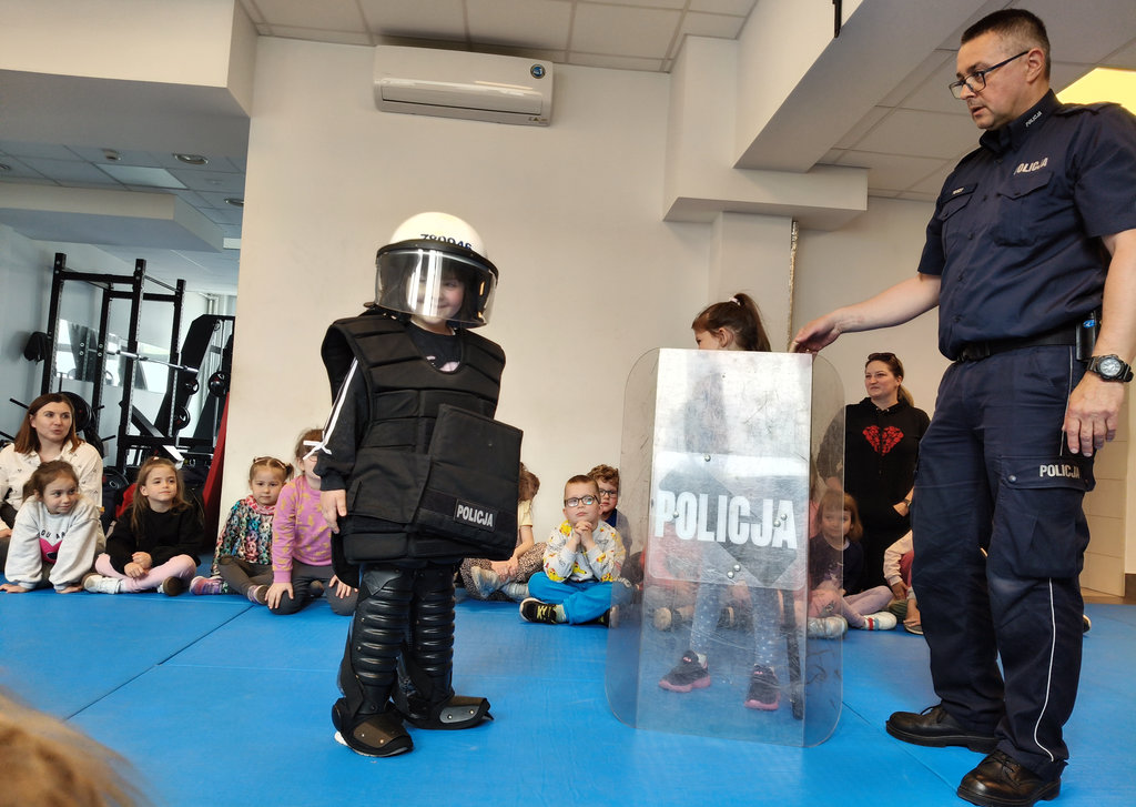 policjant i dzieci w czasie spotkania profilaktycznego, dzieci przymierzają policyjny sprzęt