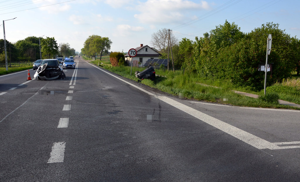 Droga krajowa, gdzie doszło do wypadku. Na jezdni stoi uszkodzone seat, w przydrożnym rowie na dachu leży osobowe audi. 