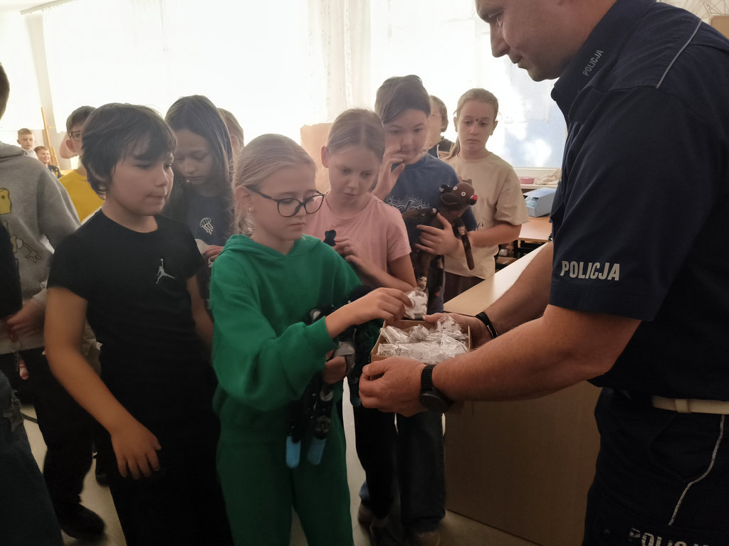 policjant rozdaje dzieciom odblaskowe breloczki
