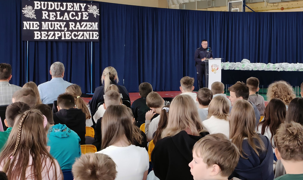 policjant za mównica mówi do uczniów, którzy siedzą na krzesłach