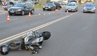 leżący na drodze motocykl biorący udział w kolizji, w tle inne pojazdy oraz  policyjny radiowóz