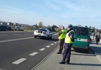 policjant i funkcjonariusz Żandarmerii Wojskowej przy cmentarzu, w tle pojazd Żandarmerii