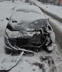 stojący na poboczu drogi zaśnieżony samochód osobowy z uszkodzonym przodem w wyniku kolizji