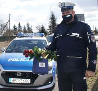 policjant obok radiowozu, w ręku trzyma kwiaty i upominki