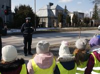 policjant stojący przed przejściem dla pieszych oraz grupa dzieci w kamizelkach odblaskowych