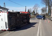 leżący na boku bus, w oddali stojący na drodze uszkodzony opel