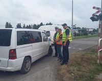 przejazd kolejowy i stojący policjant oraz funkcjonariusz Służby Ochrony Kolei w czasie kontroli drogowej