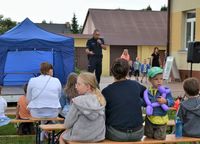 policjant w czasie spotkania profilaktycznego, ze sceny mówi do siedzących na ławkach dzieci i ich opiekunów