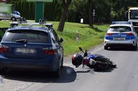 miejsce kolizji, stojące na poboczu BMW, leżący obok motorower, w tle radiowóz policyjny