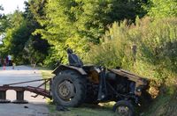 stojący na poboczu ciągnik rolniczy z podczepioną kosiarką rotacyjną, który uderzył w skarpę