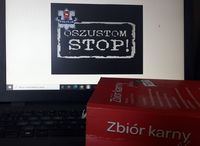 leżący na klawiaturze laptopa zbiór przepisów karnych.  Na ekranie laptopa napis oszustom stop