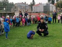 policjant pokazuje dziecku w jaki sposób należy wykonać pozycję żółwia, w tle grupa przedszkolaków