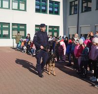 policjant z psem służbowym idący wzdłuż ustawionych w grupie  dzieci