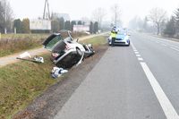 miejsce wypadku, w przydrożnym rowie stoi rozbity osobowy volkswagen, na ulicy stoi policyjny radiowóz przed nim policjant w kamizelce odblaskowej