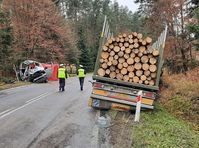 droga, miejsce tragicznego wypadku, ulicą idą dwaj policjanci, w rowie stoi rozbity bus, po przeciwnej stronie również w przydrożnym rowie tył samochodu ciężarowego z przewożonym drewnem.