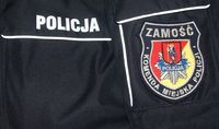 Naszywka na rękawie kurtki z logo Komendy Miejskiej Policji w Zamościu, napis Policja na kieszeni policyjnej kurtki
