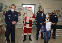 zdjęcie z finału konkursu plastycznego, I Zastępca Komendanta Miejskiego Policji w Zamościu oraz Naczelnik Ruchu Drogowego oraz dyrektor WORD w Zamościu, Mikołaj i laureatka konkursu w tle na sztalugach prace plastyczne oraz baner Komendy Miejskiej Policji w Zamościu