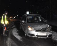 stojący na ulicy policjant kierujący ruchem, obok uszkodzony w wyniku kolizji osobowy opel