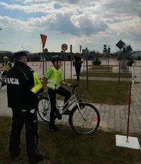 Stojący tyłem policjant i rowerzysta na terenie miasteczka ruchu drogowego podczas Turnieju Bezpieczeństwa Ruchu Drogowego