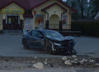 Stojąca na sklepowym parkingu uszkodzona w wyniku wypadku osobowa honda, w tle budynek sklepu. Na poboczu porozrzucany gruz - resztki betonowego przepustu, w który uderzył kierujący hondą