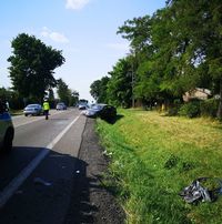 Droga i pobocze. Na jezdni stoi policjant, który kieruje ruchem. Na poboczu stoi osobowa toyota uszkodzona w wyniku wypadku.