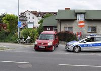 stojący na skrzyżowaniu ulic samochód osobowy marki Peugeot i policyjny radiowóz. Oparty o ogrodzenie posesji  rower.