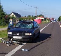 Miejsce wypadku drogowego, volkswagen z rozbitą przednią szybą, przed pojazdem leży uszkodzony rower. W tle radiowóz policyjny i wóz strażacki.