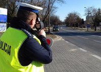 Stojący na skraju jezdni policjant mierzący prędkość jazdy kierujących