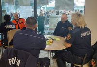 siedzący przy stolikach ratownik medyczny, policjanci oraz Straż Miejska w czasie EduTargów