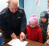 Policjant w czasie spotkania profilaktycznego pokazuje dziecku w jaki sposób daktyloskopuje się osobę.