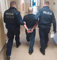 Idący tyłem dwaj policjanci z zatrzymanym mężczyzną