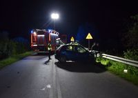 miejsce wypadku śmiertelnego. Droga i stojący w poprzek jezdni osobowy Fiat, z tyłu stoi wóz strażacki. Przy samochodzie stoją policjanci oraz dwaj mężczyźni.