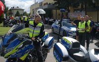 policjant na motocyklu, obok stoi drugi policyjny motocykl oraz radiowóz. W tle kolarze tuż przed startem