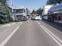 miejsce kolizji drogowej - na drodze stoją dwa samochody ciężarowe a pomiędzy nimi uszkodzony samochód osobowy koloru białego