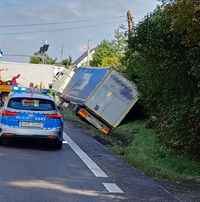 pojazd ciężarowy z naczepą w przydrożnym rowie, na drodze stoi policyjny radiowóz