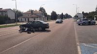 miejsce wypadku drogowego, na ulicy leży przewrócony i uszkodzony motocykl, za nim w poprzek drogi jest ustawiony pojazd marki Audi, w tle stoi radiowóz