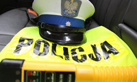 Czapka policjantów ruchu drogowego leżąca na odblaskowej  kamizelce z napisem Policja. Na kamizelce położony jest również alkomat.