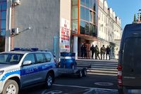przed budynkiem urzędu stoją policjanci, na placu stoi pojazd policji z beczką pirotechniczną