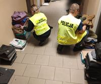 policjant i funkcjonariusz Służby Celno - Skarbowej w czasie przeliczania zabezpieczonej podrobionej odzieży, która leży na podłodze korytarza