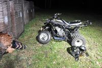 uszkodzony w wyniku zdarzenia pojazd typu quad stojący na trawie, obok pojazdu leżą dwa kaski, po lewej stronie znajdują się składowane materiały budowlane