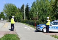 dwoje policjantów i radiowóz zaparkowany w okolicach drogi. Policjant mierzy prędkość jazdy.