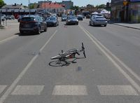 Ulica, miejsce potrącenia rowerzysty. Na ulicy leży rower, w tle  pojazd marki Kia i inne samochody jadące ulicą.