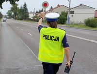 na poboczu drogi stoi  odwrócona tyłem policjantka w kamizelce odblaskowej